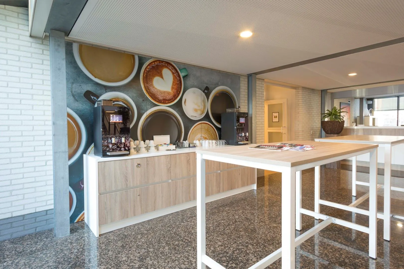 Moderne koffiecorner in een kantoorruimte aan de Steenovenweg 5, met koffiemachines, houten kasten en een wanddecoratie van koffiekopjes.