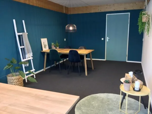 Moderne kantoorruimte aan de Steenovenweg 5 met houten vergadertafel, donkergroene muur en sfeervolle planteninrichting.
