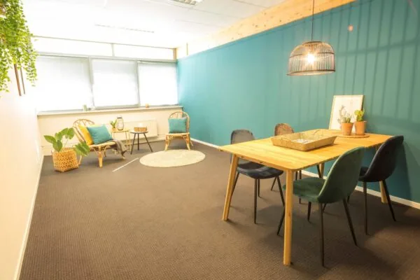 Modern ingerichte kantoorruimte aan de Steenovenweg 5-6 met een zithoek, houten vergadertafel en groene accentmuur.
