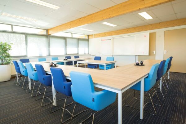 Moderne vergaderruimte op Steenovenweg 5-7 met U-vormige opstelling, blauwe stoelen en natuurlijk daglicht.