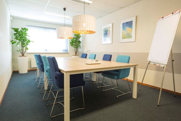 Vergaderruimte met moderne inrichting, blauwe stoelen, flip-over en grote ramen op Steenovenweg 5-9.