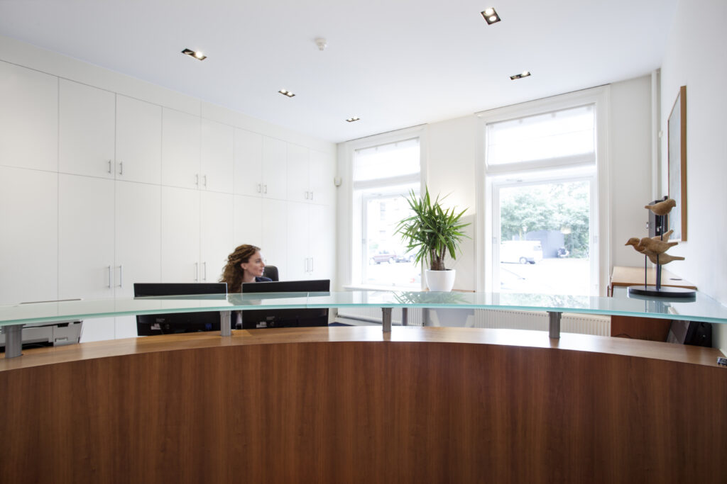 Moderne ontvangstruimte met houten balie, glazen blad en een receptioniste bij kantoorruimte Sweelinckplein 1-3.