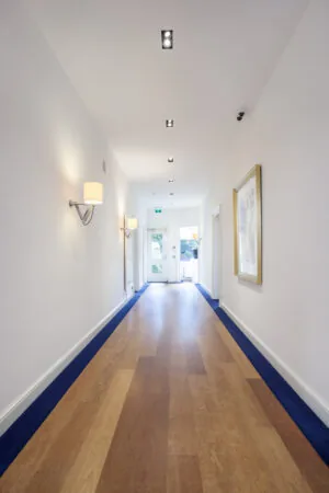 Verlichte gang met houten vloer, witte muren en moderne wandlampen in kantoorruimte Sweelinckplein 1-6.