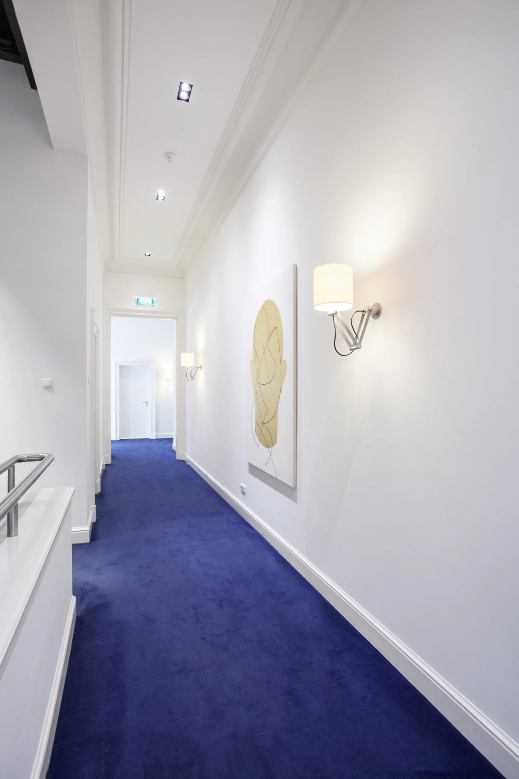 Lichte gang met blauw tapijt en moderne wandverlichting in kantoorruimte op Sweelinckplein 1-7.
