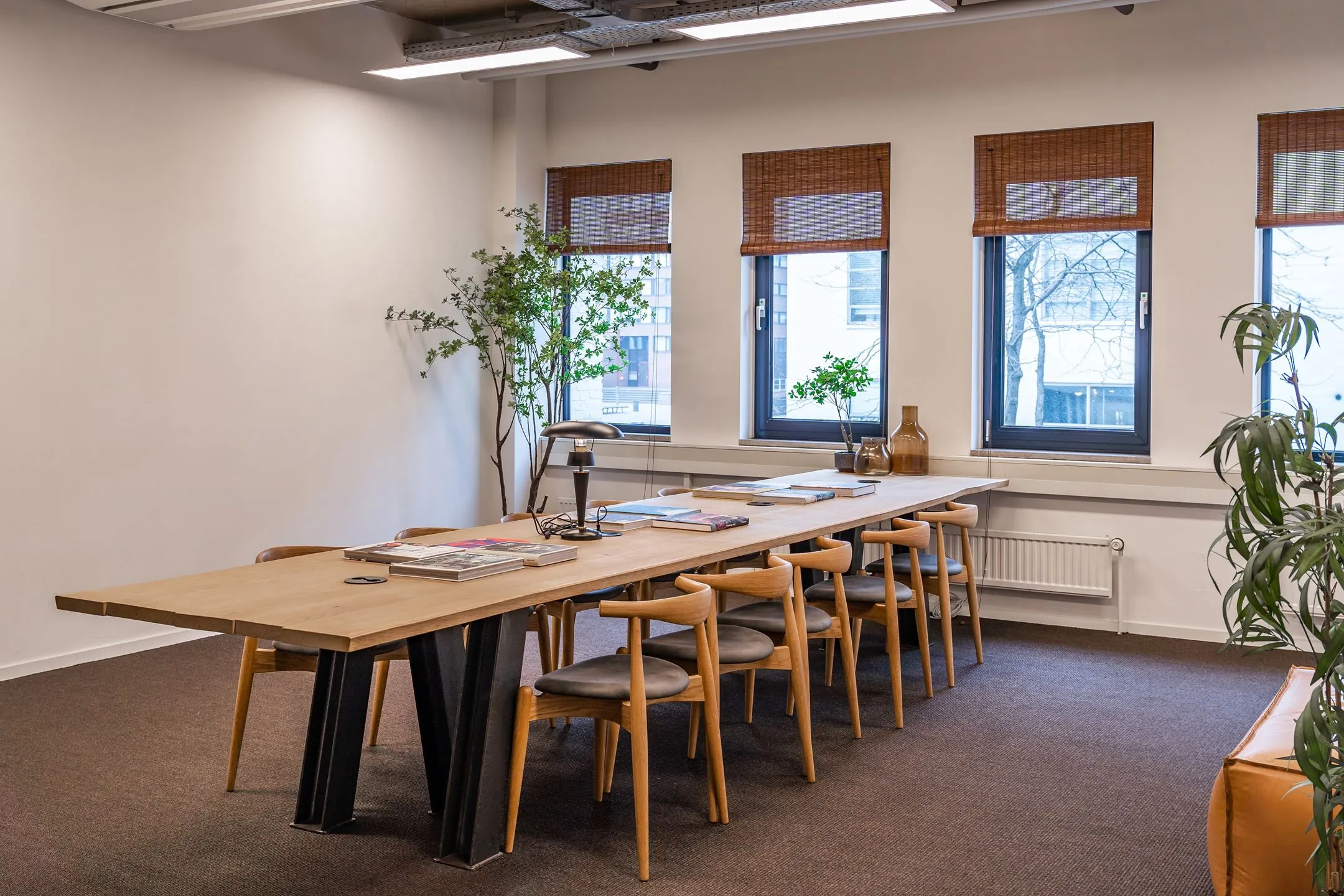 Moderne vergaderruimte aan de Emmasingel 33 met een lange houten tafel, designstoelen en grote ramen met jaloezieën.
