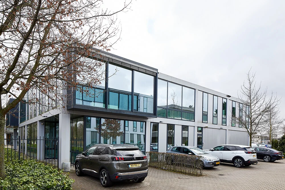 Modern kantoorgebouw aan de Floridadreef 112 met grote ramen en parkeerplaatsen voor de deur.