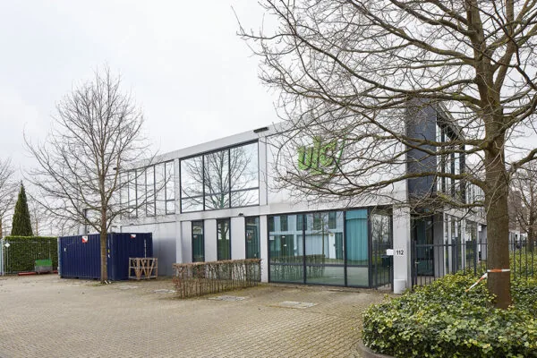 Modern kantoorgebouw aan de Floridadreef 112 met grote ramen en omringende bomen.