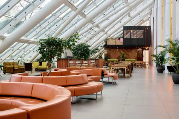 Moderne, lichte kantoorruimte aan de Johan Huizingalaan 400 met oranje zitbanken, veel groen en houten werkplekken.