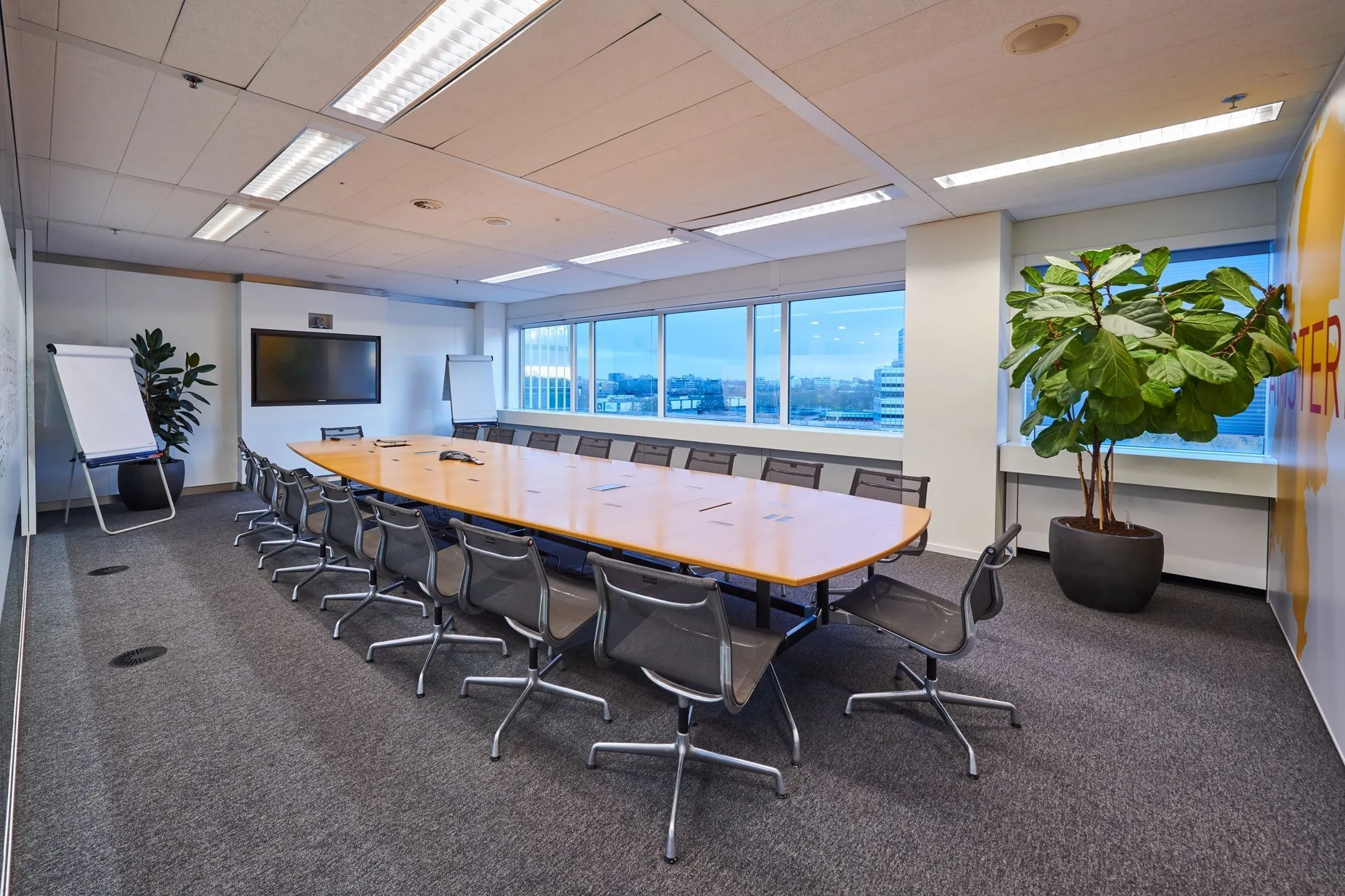 Vergaderruimte met lange tafel, moderne stoelen, flip-overs en groot scherm in kantoor aan Johan Huizingalaan 400.