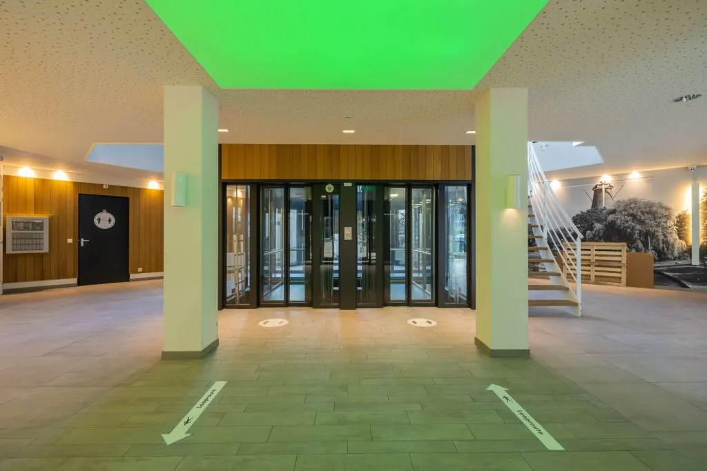 Inkomhal van kantoorpand aan de Schipholweg 55 in Leiden met glazen draaideuren, trap en wandfoto van een molen.