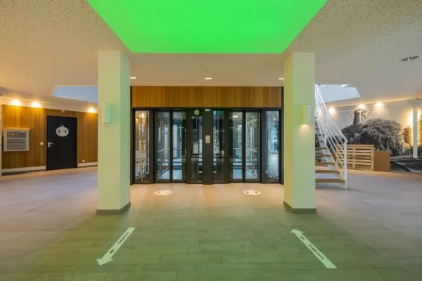 Inkomhal van kantoorpand aan de Schipholweg 55 in Leiden met glazen draaideuren, trap en wandfoto van een molen.