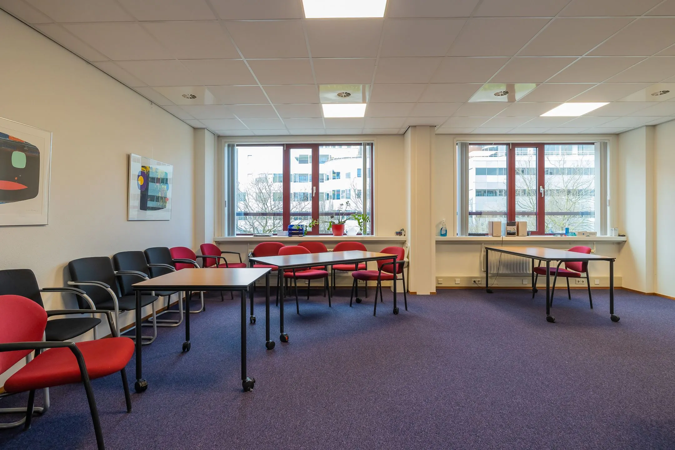 Vergader- of kantoorruimte in Leiden aan de Schipholweg 55 met tafels, stoelen en grote ramen met uitzicht op kantoorpanden.
