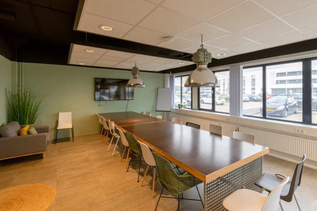 Moderne vergaderruimte op Reactorweg 301 met grote tafel, diverse stoelen, flatscreen en uitzicht op parkeerterrein.