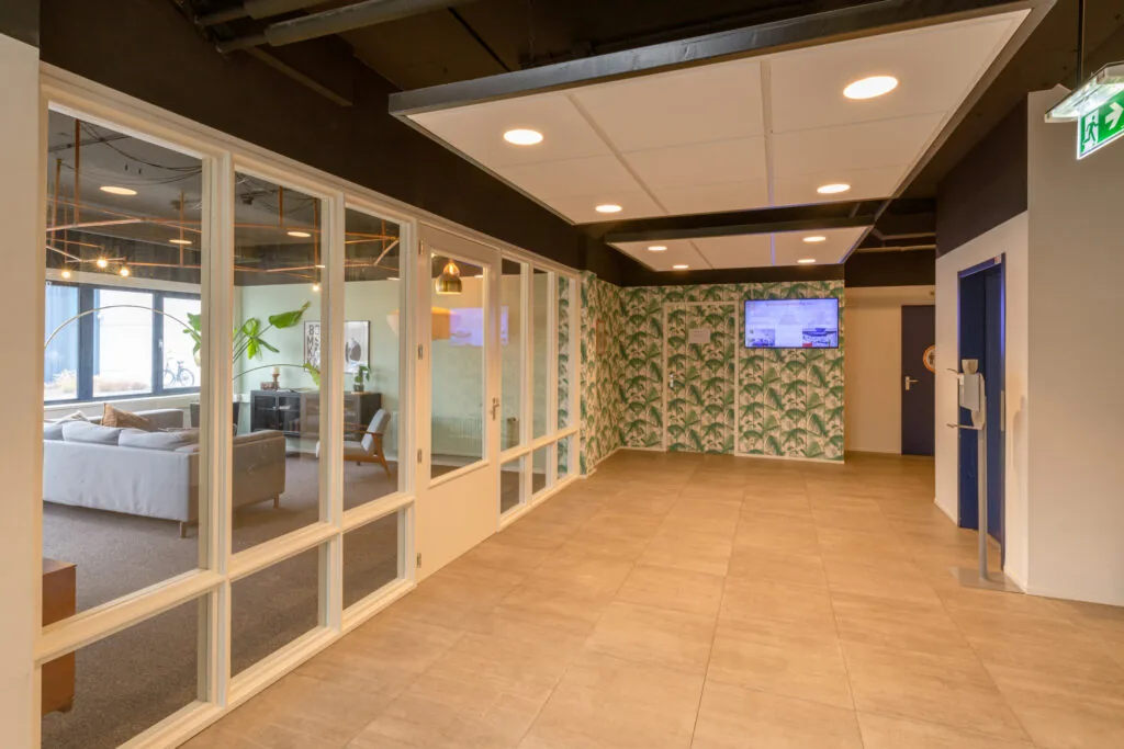 Moderne entreehal van kantoorruimte Reactorweg 301 met glazen wanden, tropisch behang en zicht op een loungegedeelte.