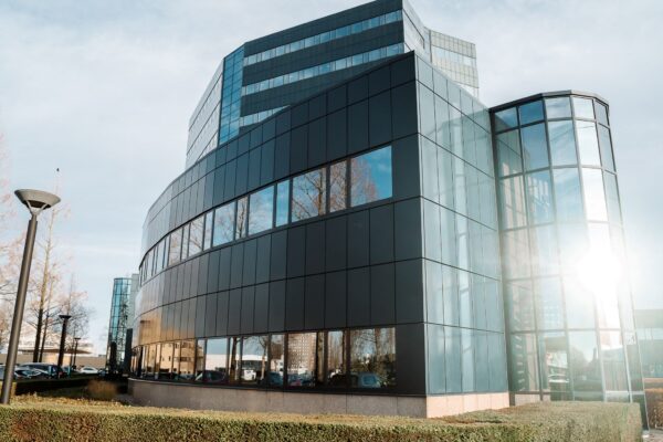 Modern kantoorgebouw aan de Reitscheweg 1 in Den Bosch met glazen gevel en spiegelende ramen.