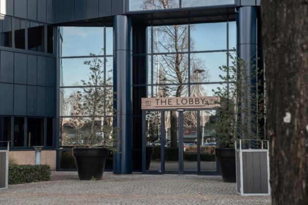 Ingang van het kantoorgebouw aan de Reitscheweg 1 met het bord “The Lobby” boven de glazen deuren.