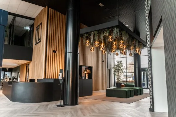 Moderne ontvangstruimte met houten wandbekleding, designverlichting en groene zitbanken in een kantoorpand aan de Reitscheweg.