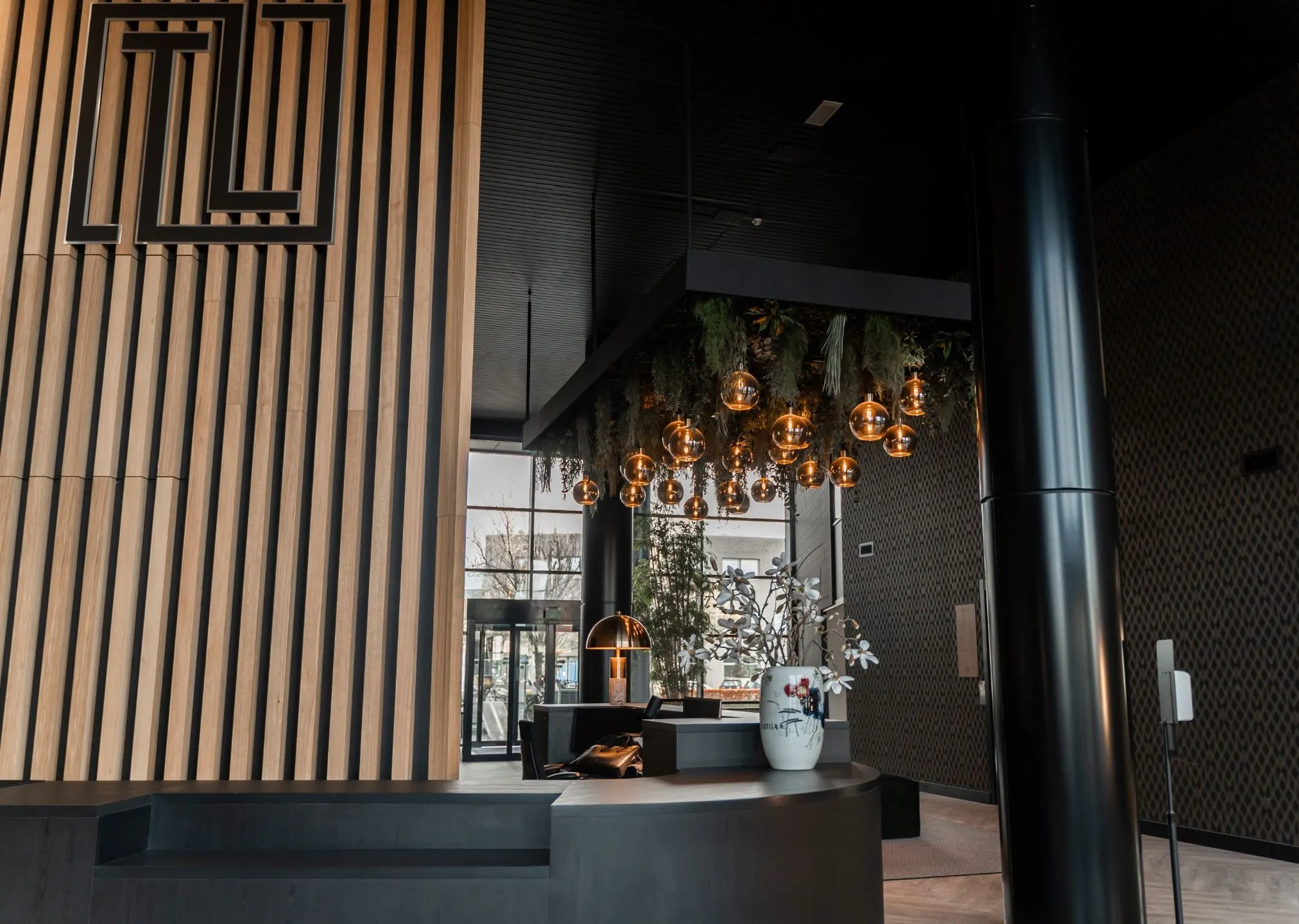 Moderne ontvangsthal van een kantoorruimte aan de Reitscheweg 1-5 met houten wandpanelen, hanglampen en een stijlvolle balie met bloemenvaas.
