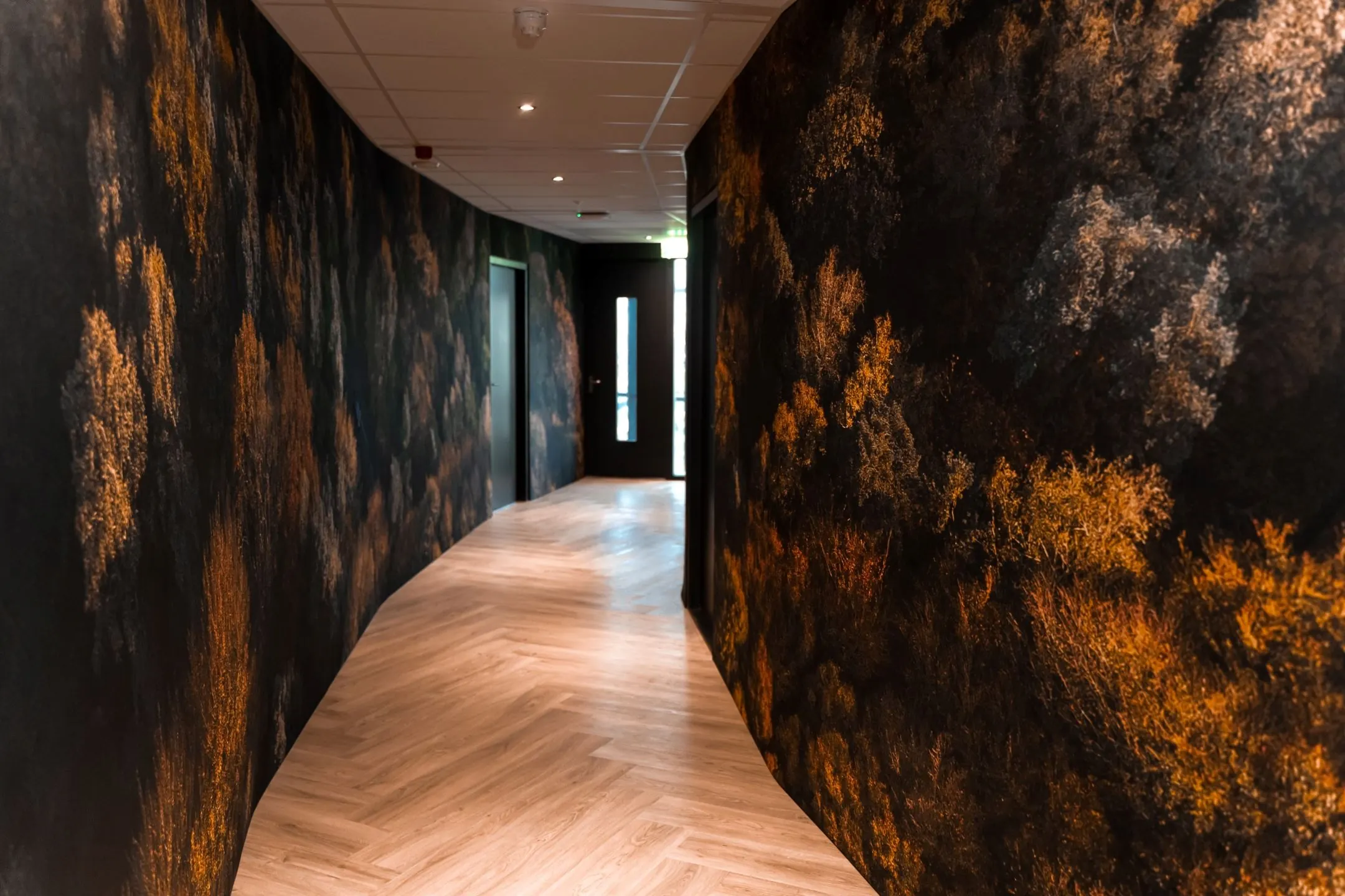 Gang met sfeervolle wanddecoratie en licht houten visgraatvloer in een kantoorruimte aan de Reitscheweg 1-7.