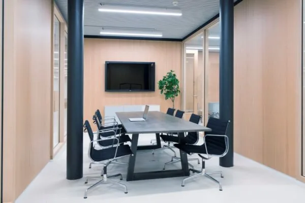 Moderne vergaderruimte aan de Wardropstraat 5 met houten wanden, een lange tafel, acht zwarte stoelen, een flatscreen en een laptop.