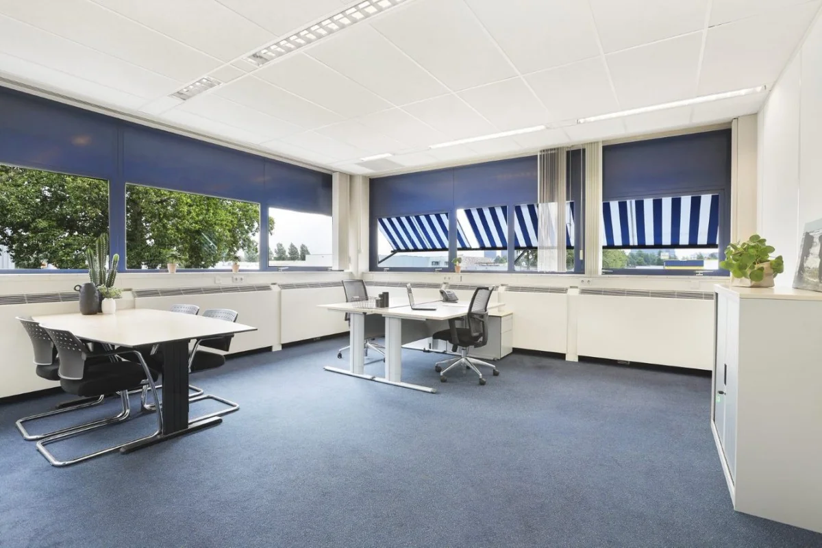 Lichte en moderne kantooruimte in Markerkant Almere met werkplekken, vergadertafel en grote ramen met blauwe zonwering.
