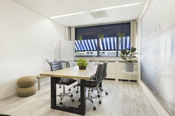 Moderne vergaderruimte in Markerkant, Almere met houten tafel, zwarte stoelen en grote ramen met blauw-witte zonwering.