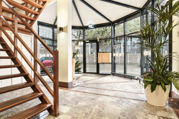 Entreehal van kantoorpand Kennemerplein 20 in Haarlem met marmeren vloer, houten trap en grote glazen gevel.