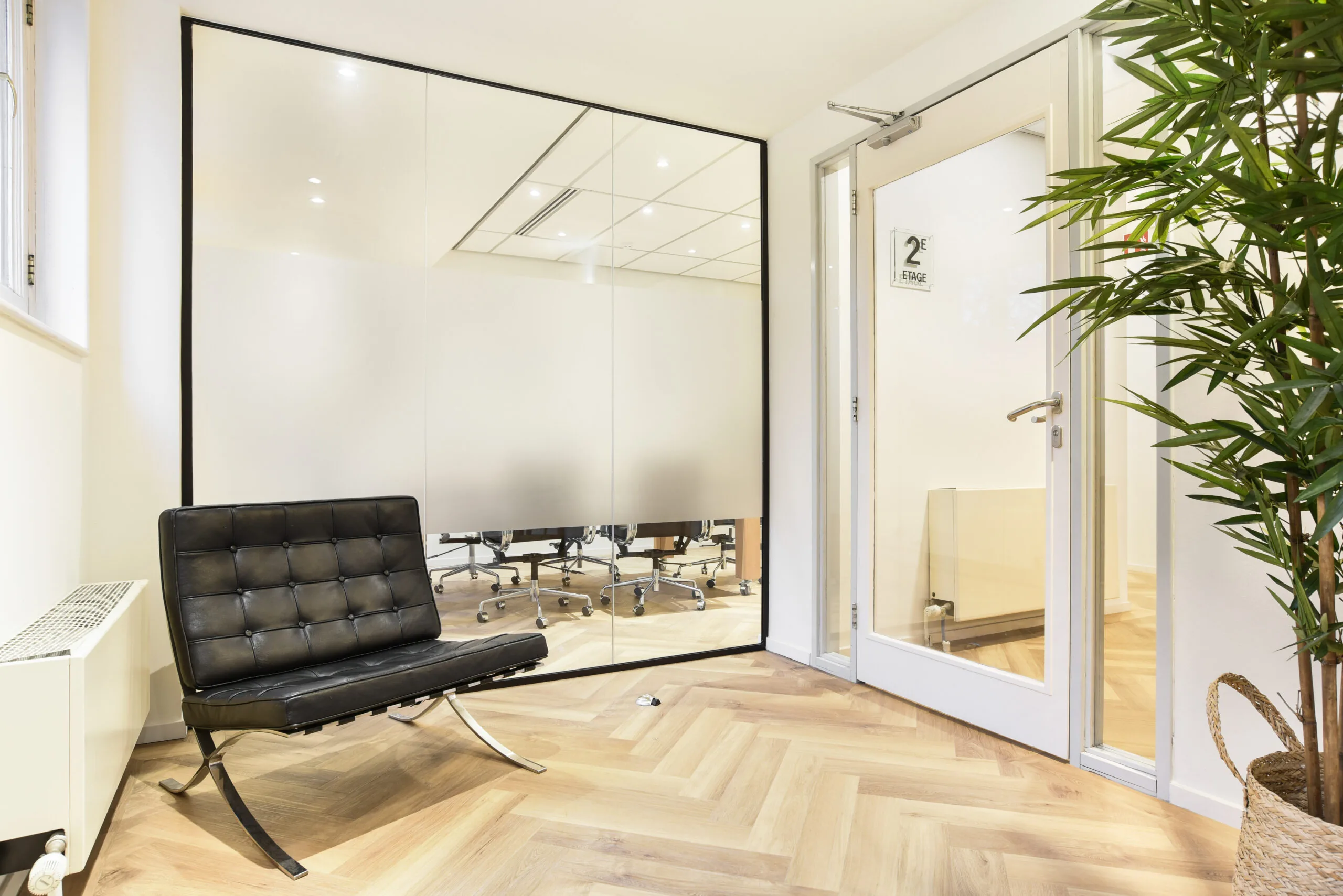 Moderne wachtruimte op de tweede etage van Kennemerplein 20 in Haarlem met designstoel, glazen wand en houten visgraatvloer.