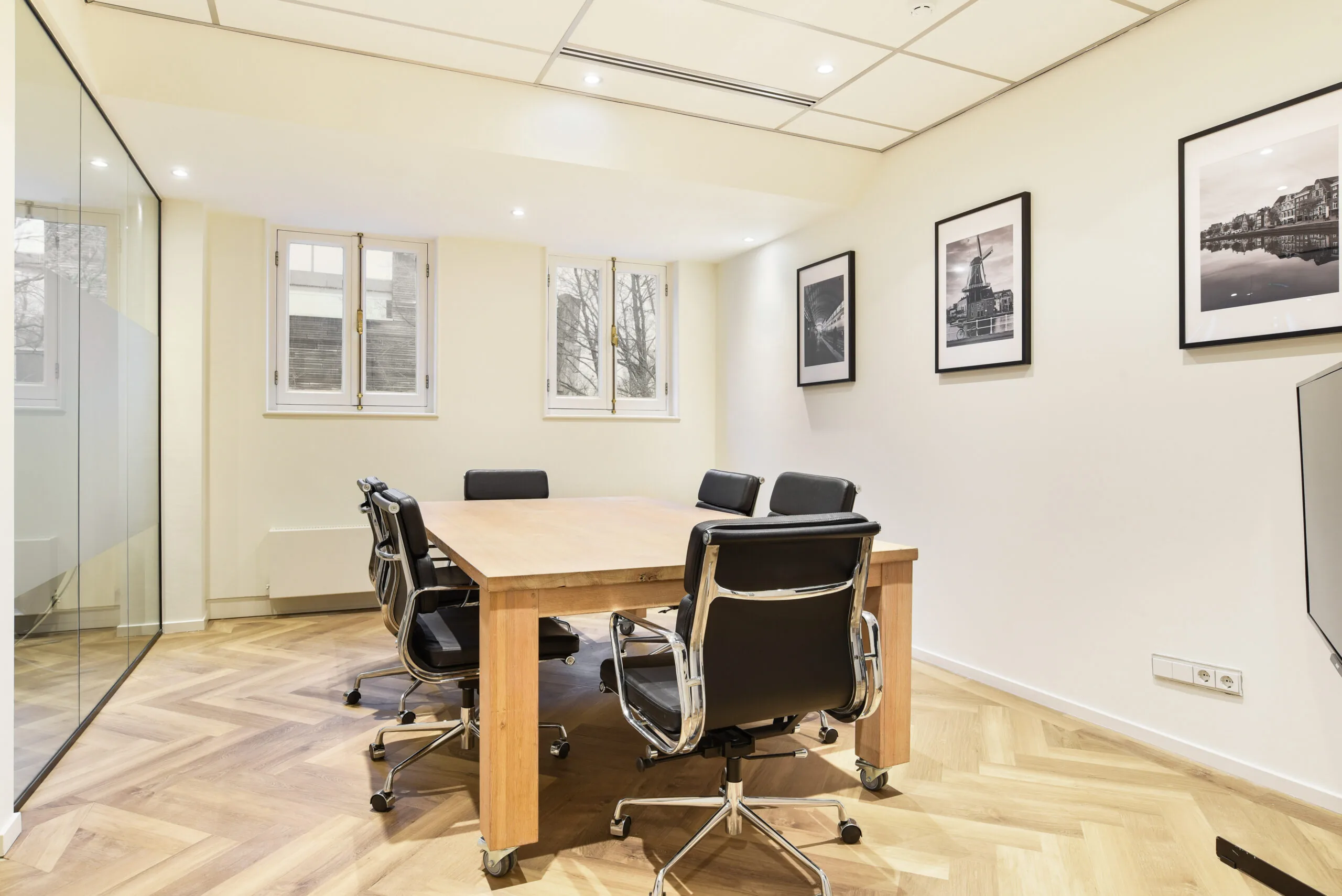 Moderne vergaderruimte met houten tafel, zes zwarte bureaustoelen en zwart-witfoto’s aan de muur in Kennemerplein 20, Haarlem.