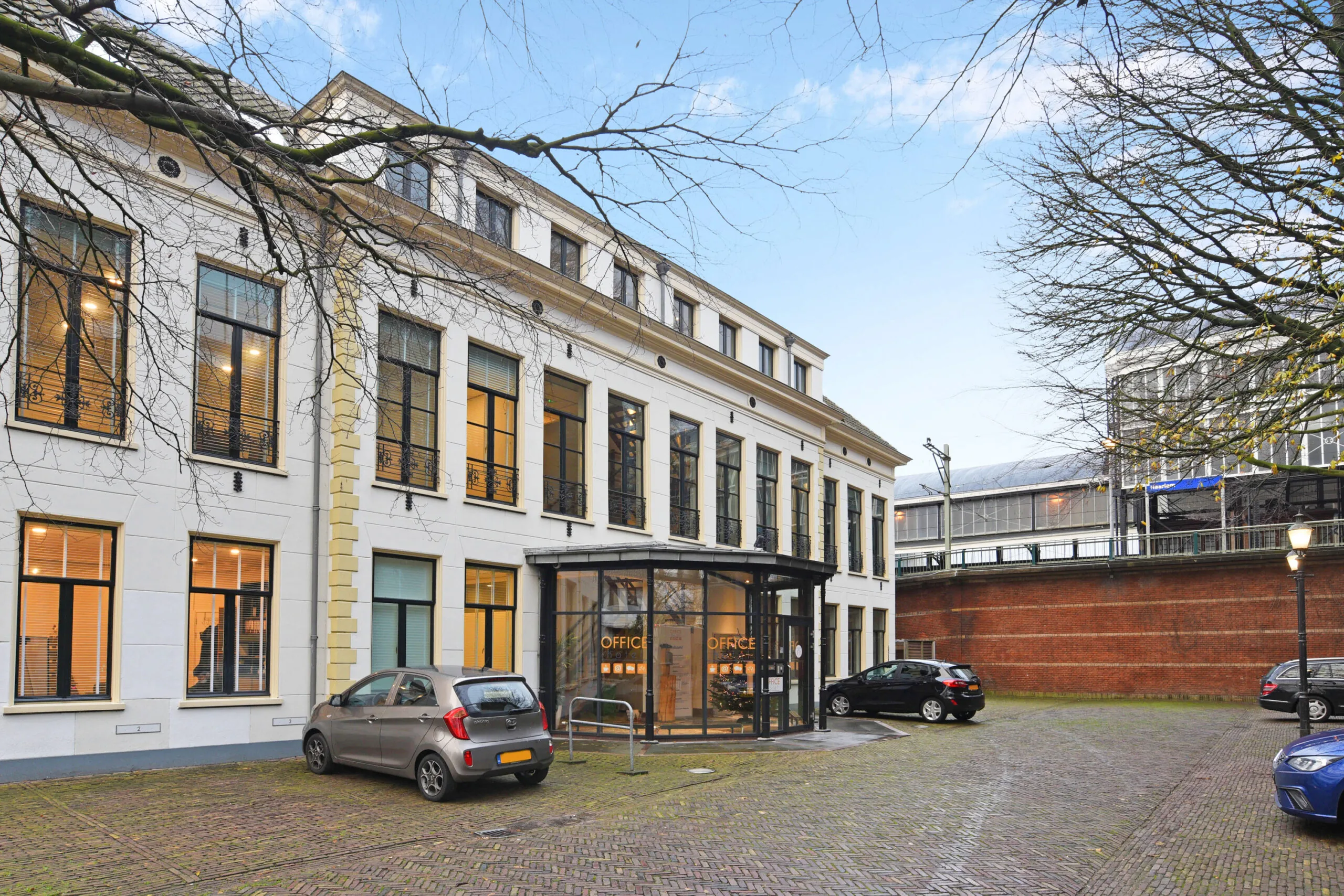 Wit kantoorpand aan het Kennemerplein 20 in Haarlem met grote ramen en geparkeerde auto's op de voorgrond.