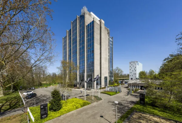Hoog kantoorgebouw Kronenburg 004 van Paul Starink met spiegelende ramen, omgeven door bomen en parkeerplaatsen op een zonnige dag.