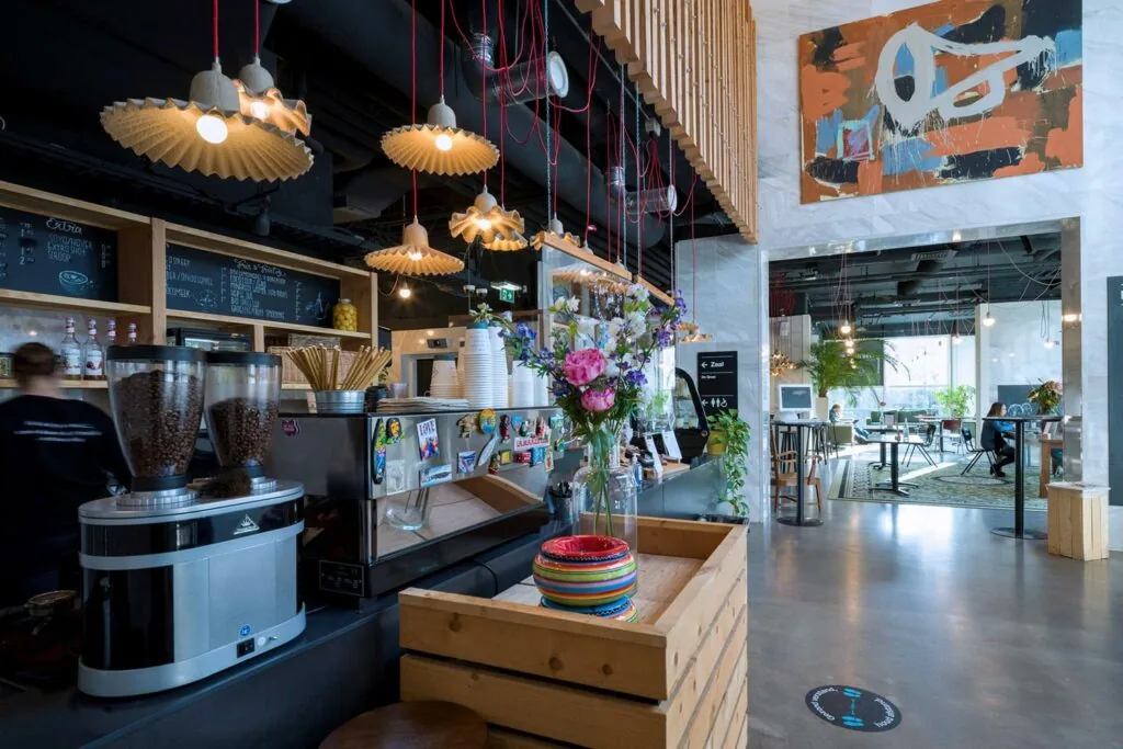 Modern ingerichte koffiebar aan de Laan van Kronenburg met een kleurrijk interieur, bloemen op de toonbank en zicht op een open zitgedeelte.