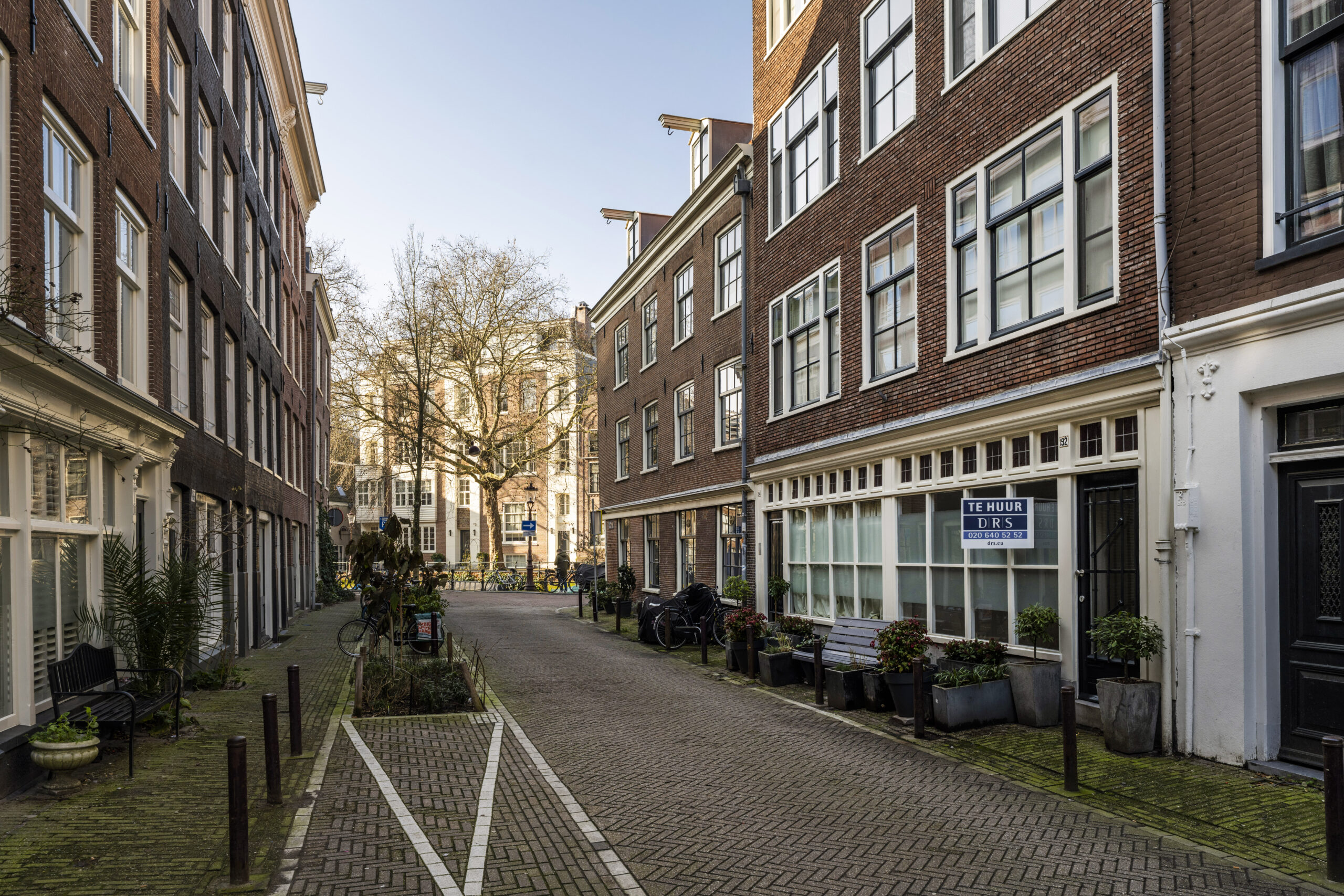 Een rustige straat in Amsterdam met klassieke bakstenen gebouwen en een "Te Huur" bord aan een van de panden aan de Leliestraat.