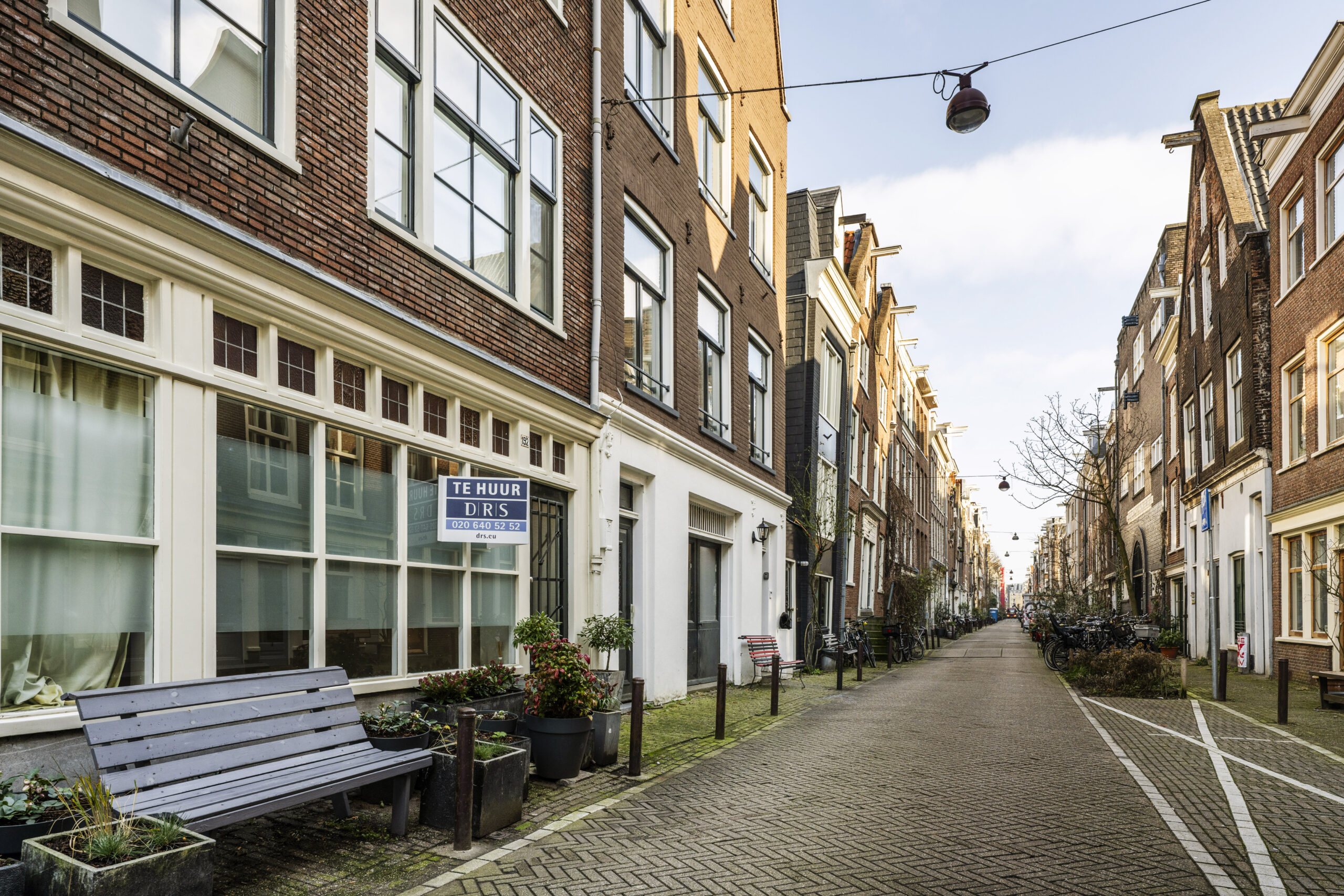 Een rustige straat met karakteristieke Amsterdamse gevels en een pand aan de Leliestraat met een 'Te Huur' bord.