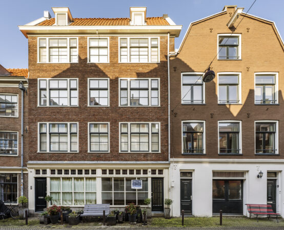 Voorgevel van een karakteristiek Amsterdams herenhuis aan de Leliestraat met grote ramen, bloembakken en een bankje.