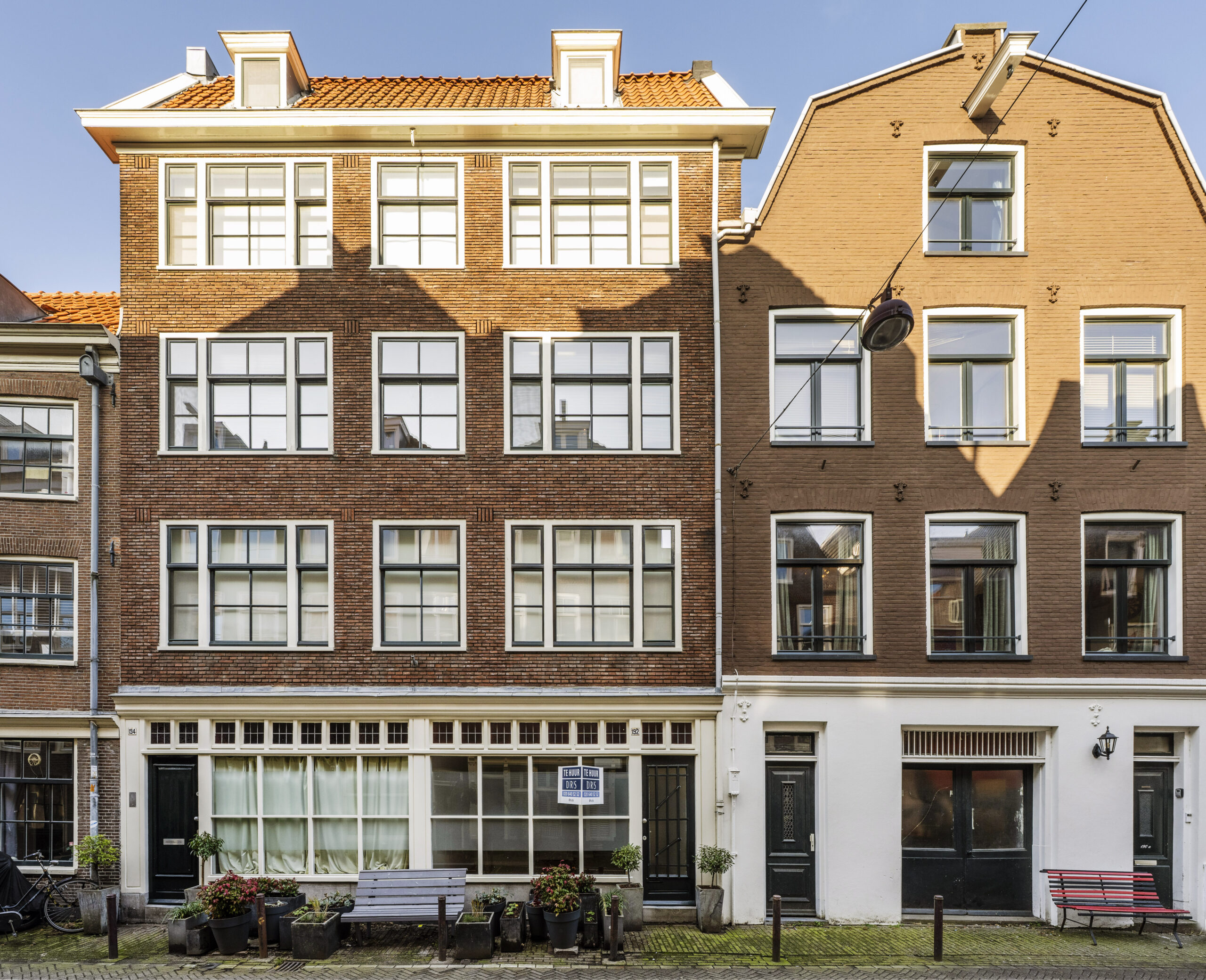Voorgevel van een karakteristiek Amsterdams herenhuis aan de Leliestraat met grote ramen, bloembakken en een bankje.