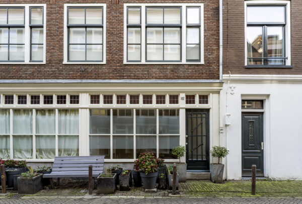 Voorgevel van een woonhuis aan de Leliestraat met grote ramen, twee deuren, een houten bank en bloembakken.