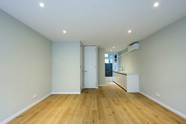 Moderne, lege woonkamer met houten vloer en open keuken in woning aan Leliestraat 013 van Paul Starink.
