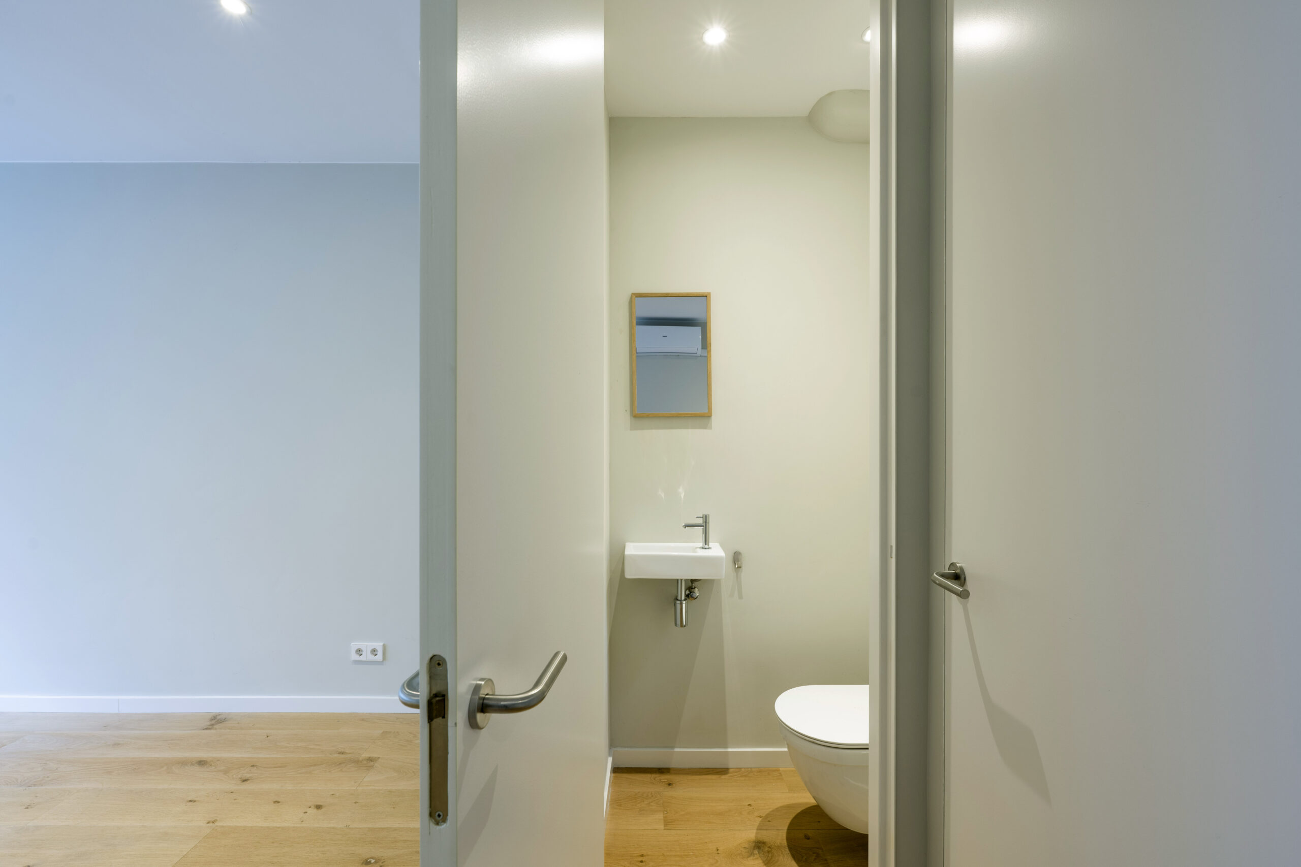 Doorkijk naar een minimalistisch toilet met wastafel en spiegel in woning aan Leliestraat.