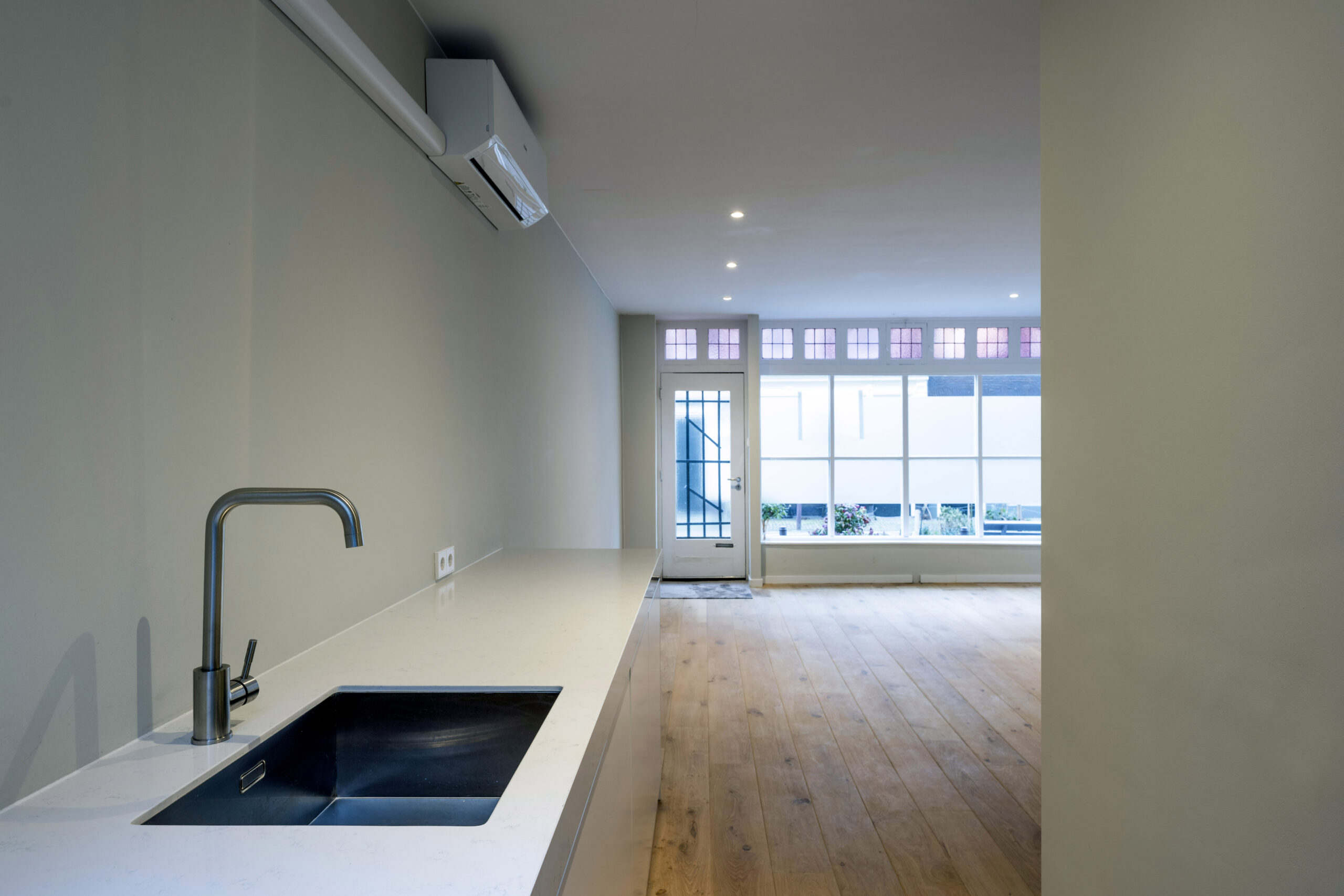 Moderne open keuken met witte werkblad en houten vloer in woning aan de Leliestraat, ontworpen door Paul Starink.