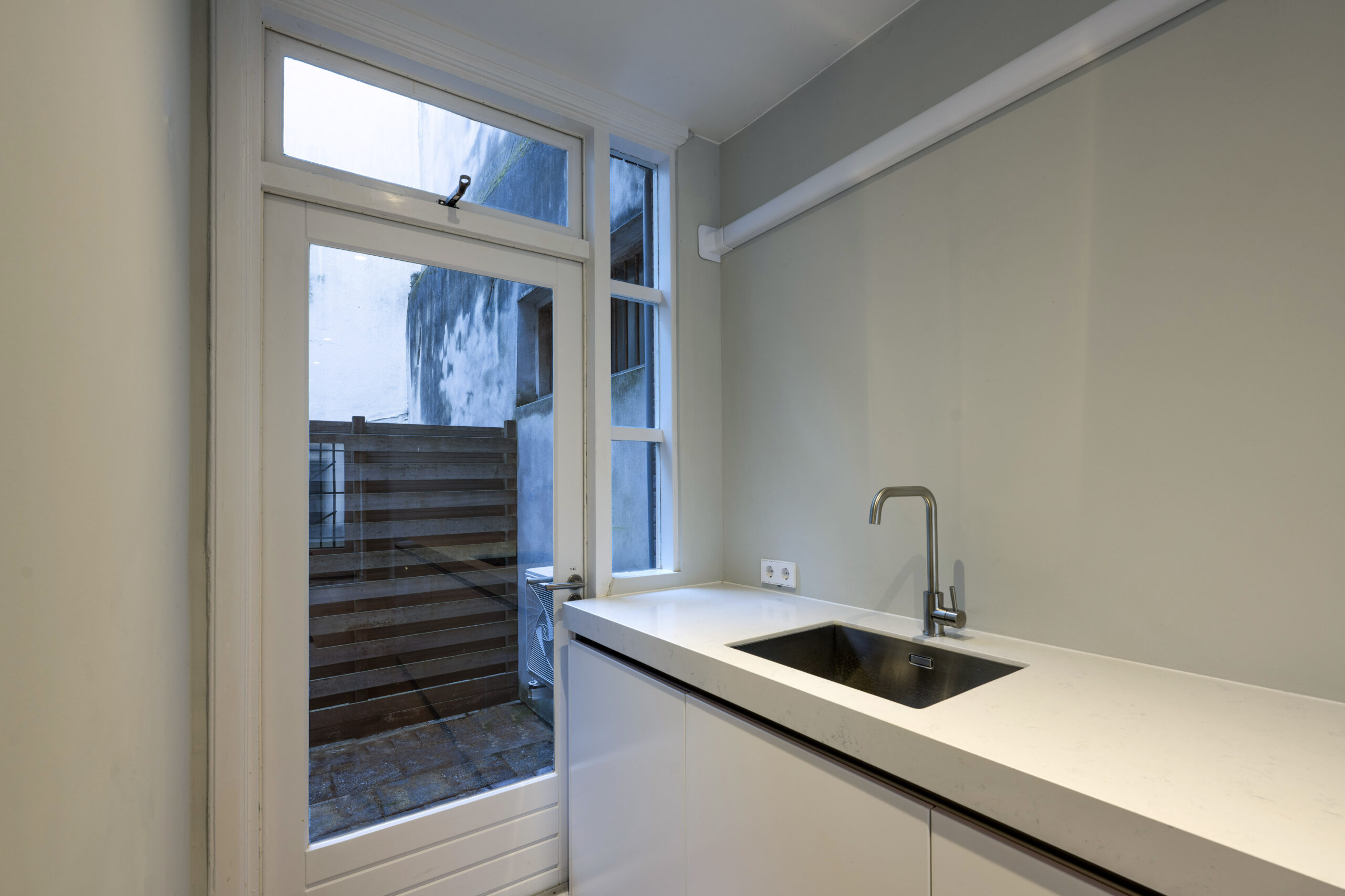 Moderne, minimalistische keuken met wit aanrechtblad en roestvrijstalen kraan aan de Leliestraat, met zicht op een kleine patio.