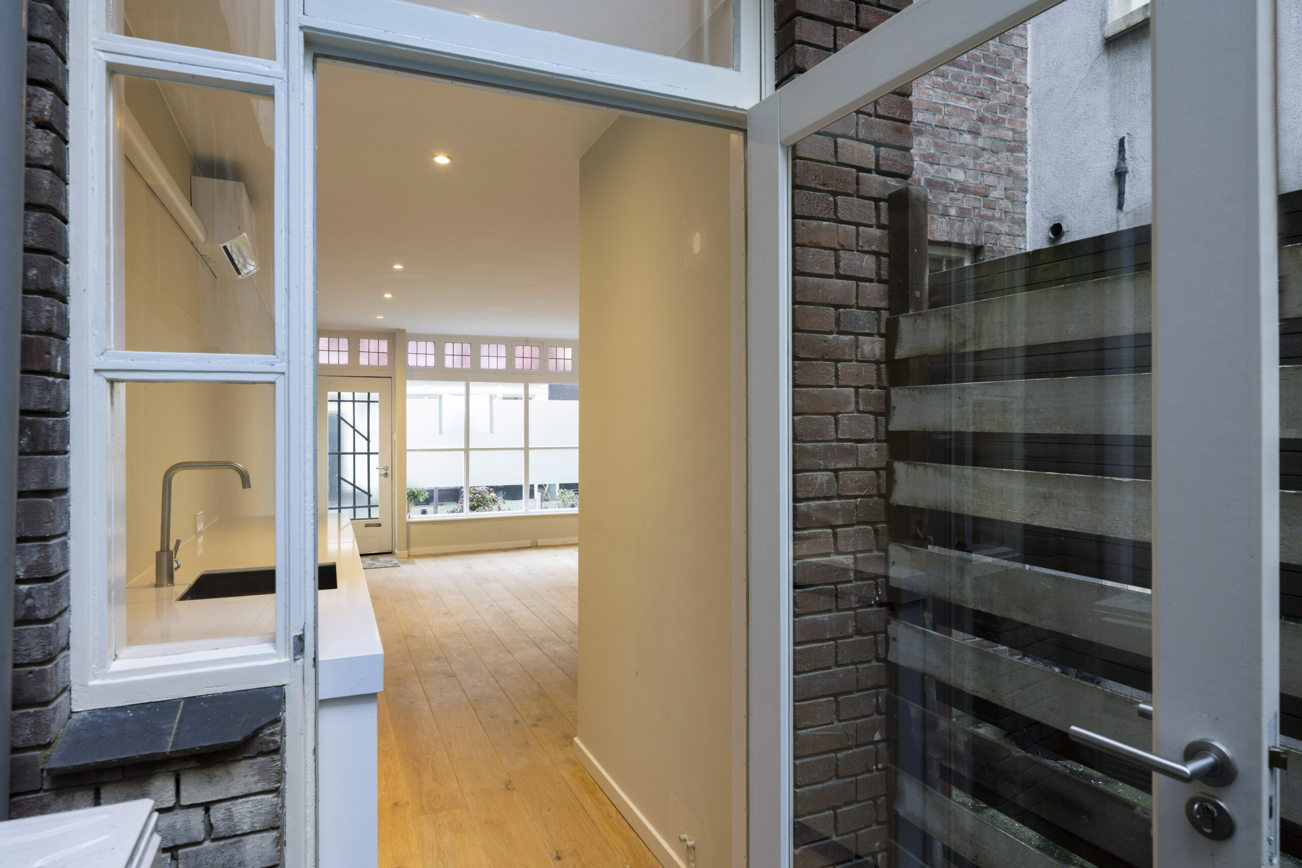 Doorkijk vanuit een kleine patio naar een lichte woonkamer met houten vloer aan de Leliestraat 024, ontworpen door Paul Starink.