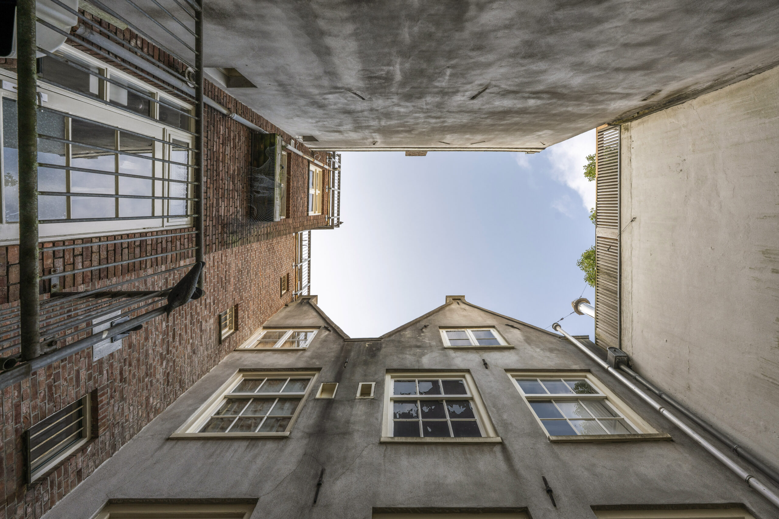Kijk omhoog in een smalle steeg tussen oude gevels aan de Leliestraat, gefotografeerd door Paul Starink.
