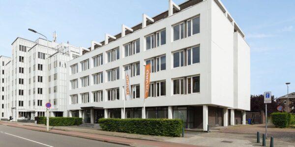 Een groot, wit kantoorpand met meerdere verdiepingen en oranje vlaggen aan de voorzijde.
