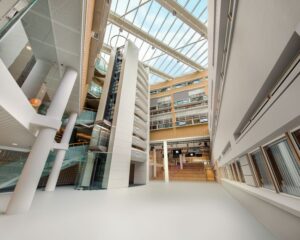 Ruime en moderne binnenhal van het gebouw M met glazen dak en meerdere verdiepingen.
