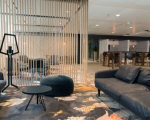 Moderne lounge met comfortabele zitplekken, een kleurrijk vloerkleed en houten latwerk als ruimteverdeler.