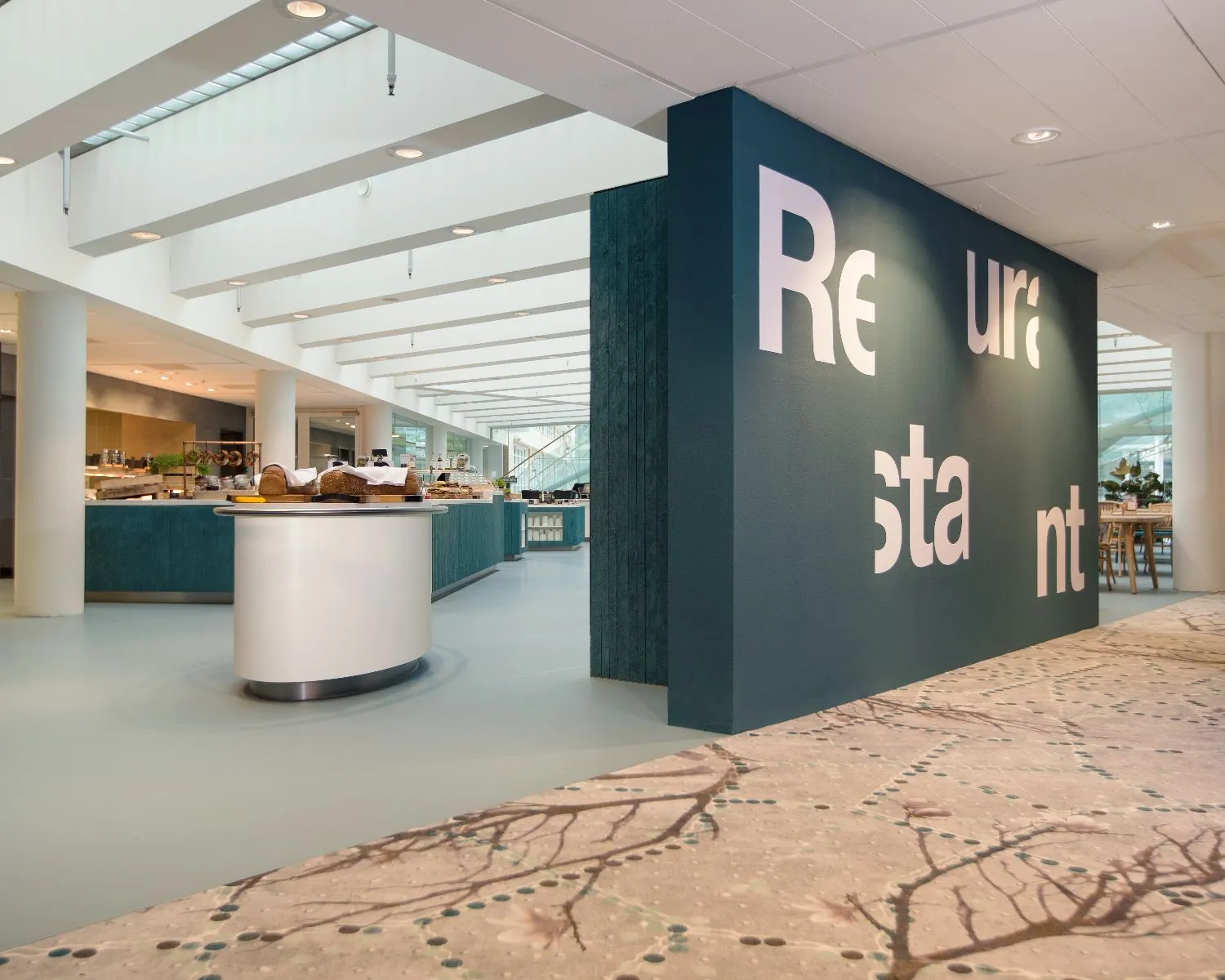 Modern restaurantinterieur met open buffetruimte en opvallende wand met het woord ‘Restaurant’ in grote letters.