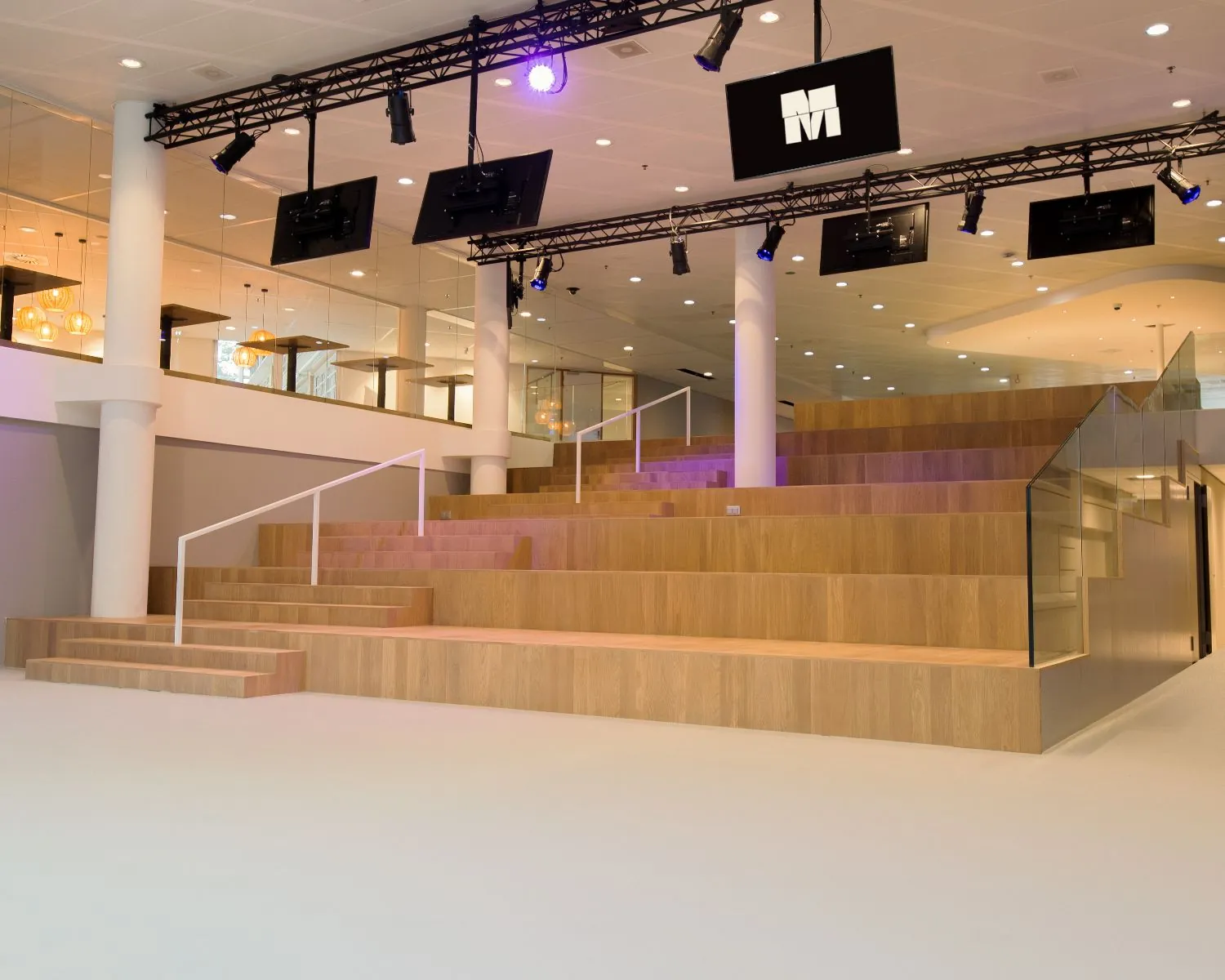 Houten tribunetrap met glazen en witte leuningen in een modern interieur van een bedrijfs- of evenementenruimte.