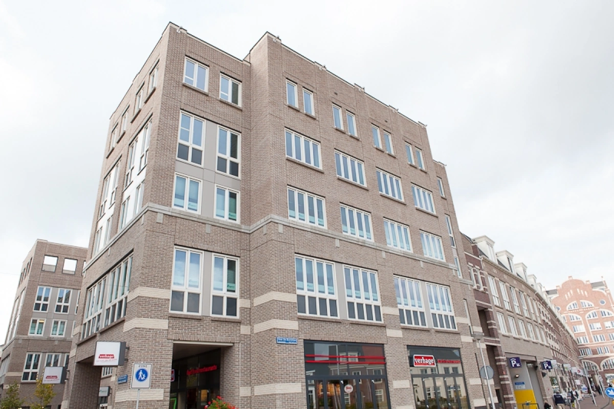 Bakstenen hoekgebouw Middenburcht 136 met winkels op de begane grond en meerdere verdiepingen met ramen.