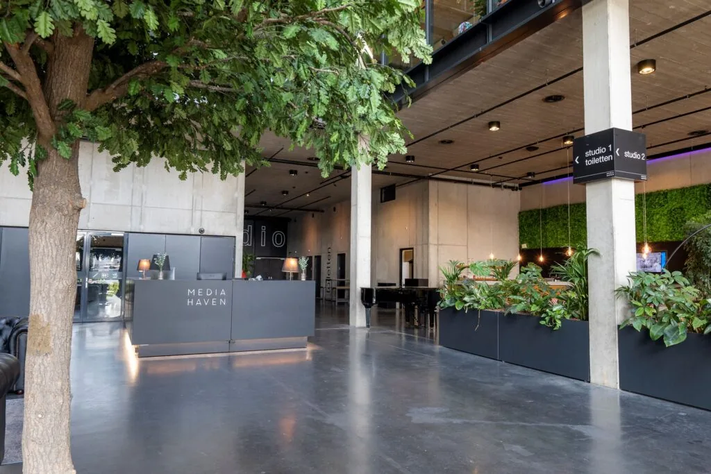 Moderne entreehal van Media Haven aan de Moermanskkade met balie, binnentuin en duidelijke bewegwijzering naar studio's.